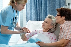 Female Nurse is smiling and holding an elderly female patients hand